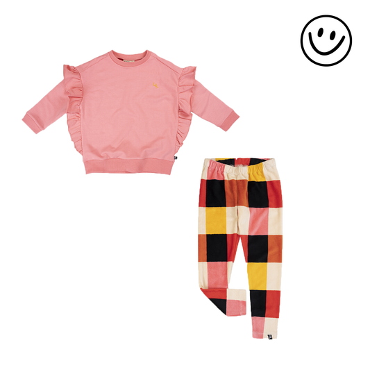 Dit is een roze trui met een ruffel aan de zijkant en een legging met een geblokte print van beige, zwart, bruin, rood en roze. 